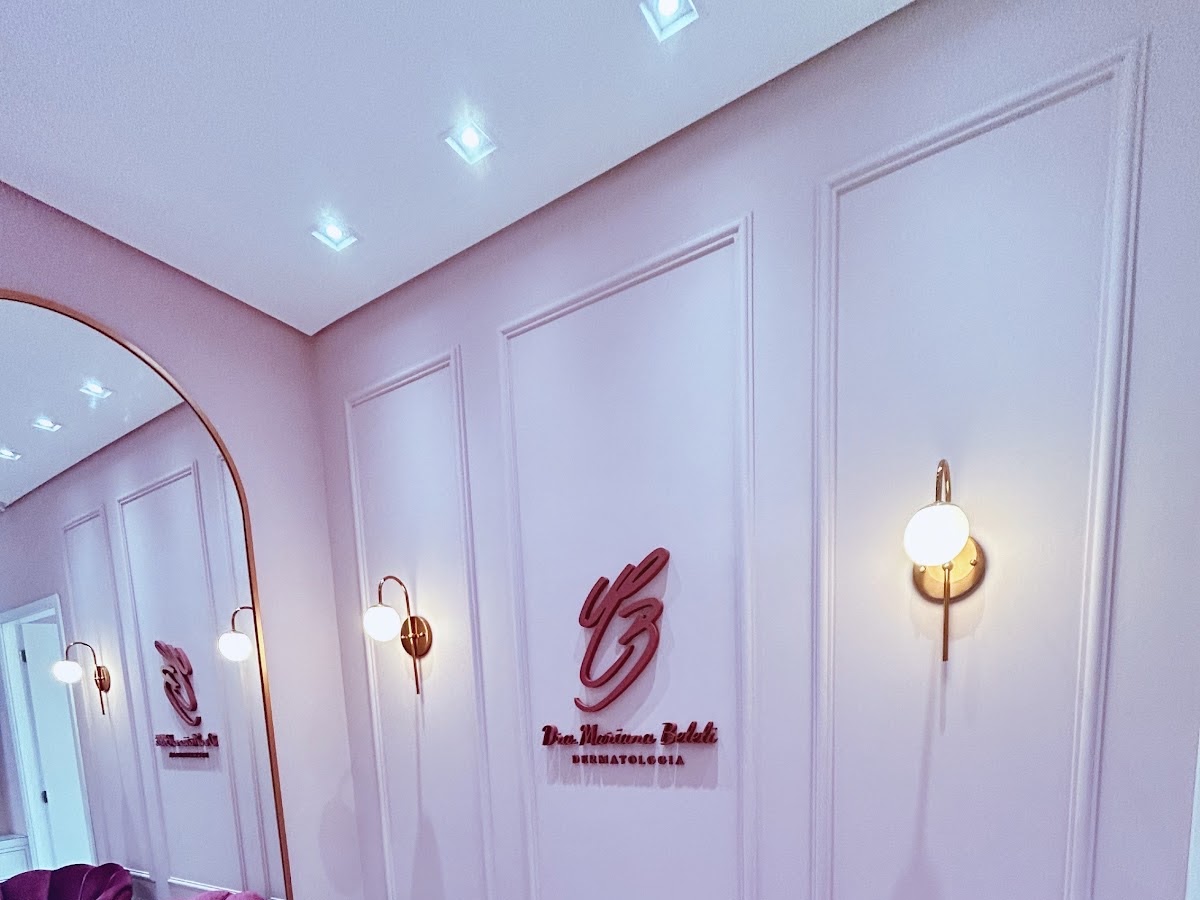 Interior do consultório da Dra. Mariana Beleli no Medplex Campinas: parede com boiserie em tom rosé-lilás, espelho arqueado com moldura dourada e arandelas acesas
